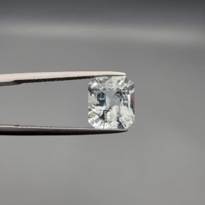​A 3.77 carat natural emerald-cut Aquamarine (Beruj) from Shigar Valley, Pakistan, displaying distinct black needle-like and "mountain" inclusions on the reverse side, held in jeweler's tweezers.