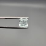 A 2.60 carat natural emerald-cut Aquamarine (Beruj) from Shigar Valley, Pakistan, held in tweezers, showing a clear face and a back side with distinct black needle-like mountain inclusions.