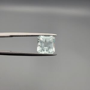 A 2.60 carat natural emerald-cut Aquamarine (Beruj) from Shigar Valley, Pakistan, held in tweezers, showing a clear face and a back side with distinct black needle-like mountain inclusions.