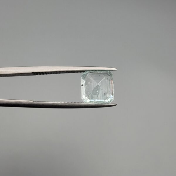 A 2.60 carat natural emerald-cut Aquamarine (Beruj) from Shigar Valley, Pakistan, held in tweezers, showing a clear face and a back side with distinct black needle-like mountain inclusions.