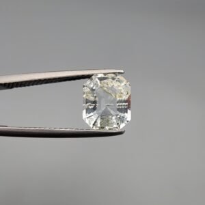 A 1.93 carat natural emerald-cut Aquamarine (Beruj) from Shigar Valley, Pakistan, held in tweezers, showing a clean face-up appearance with unique yellow and black mountain-like inclusions and natural surface pits on the reverse.