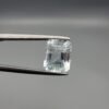 ​A 2.39 carat natural emerald-cut Aquamarine (Beruj) from Shigar Valley, Pakistan, held in jeweler's tweezers, showing a pale blue transparency with visible internal natural inclusions.