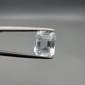 ​A 2.39 carat natural emerald-cut Aquamarine (Beruj) from Shigar Valley, Pakistan, held in jeweler's tweezers, showing a pale blue transparency with visible internal natural inclusions.