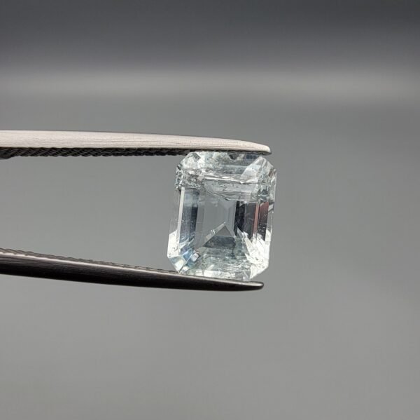 ​A 2.39 carat natural emerald-cut Aquamarine (Beruj) from Shigar Valley, Pakistan, held in jeweler's tweezers, showing a pale blue transparency with visible internal natural inclusions.