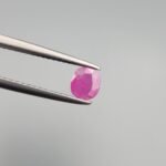 A 0.43 carat natural pinkish-red Ruby (Yaqoot) from Kabul, Afghanistan, featuring a classic cushion cut with visible internal natural silk and inclusions, held in jeweler's tweezers.