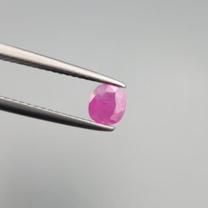 A 0.43 carat natural pinkish-red Ruby (Yaqoot) from Kabul, Afghanistan, featuring a classic cushion cut with visible internal natural silk and inclusions, held in jeweler's tweezers.
