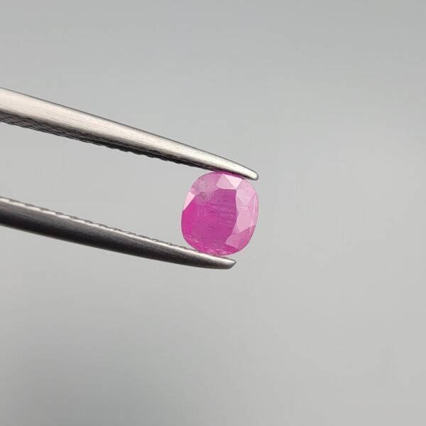 A 0.43 carat natural pinkish-red Ruby (Yaqoot) from Kabul, Afghanistan, featuring a classic cushion cut with visible internal natural silk and inclusions, held in jeweler's tweezers.