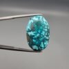 A 25-carat natural Iranian Turquoise (Feroza) from Kerman City, featuring a large oval cabochon cut with a vibrant blue-green base and dense golden pyrite matrix, held in jeweler's tweezers.