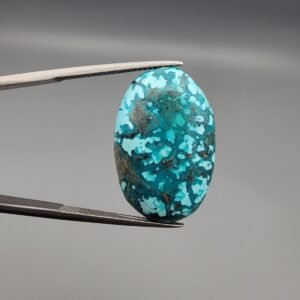 A 25-carat natural Iranian Turquoise (Feroza) from Kerman City, featuring a large oval cabochon cut with a vibrant blue-green base and dense golden pyrite matrix, held in jeweler's tweezers.