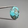 A 37.23-carat natural Iranian Turquoise (Feroza) from Kerman City, featuring a substantial oval cabochon cut with a vibrant sky-blue base and a heavy golden pyrite matrix, held in jeweler's tweezers.