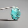 A 37.23-carat natural Iranian Turquoise (Feroza) from Kerman City, featuring a substantial oval cabochon cut with a vibrant sky-blue base and a heavy golden pyrite matrix, held in jeweler's tweezers.