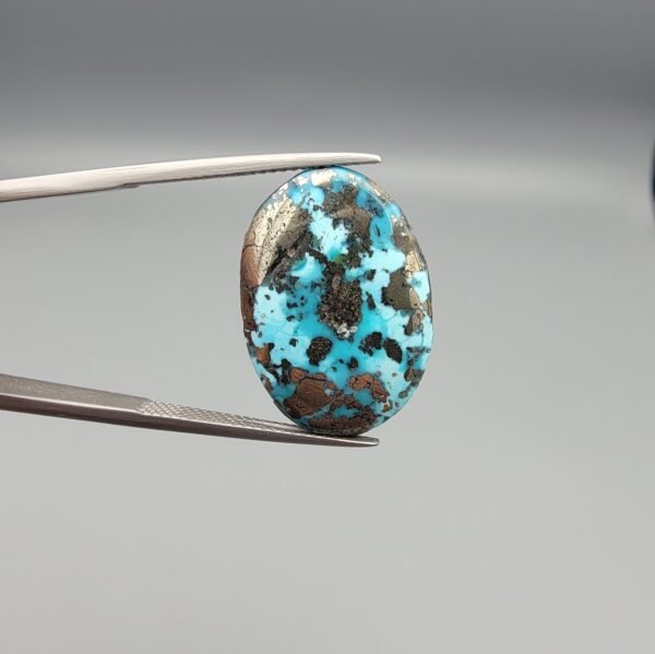 ​A 24.62-carat natural Iranian Turquoise (Feroza) from Kerman City, featuring a large oval cabochon cut with a vivid blue base and a beautiful web of metallic pyrite inclusions.