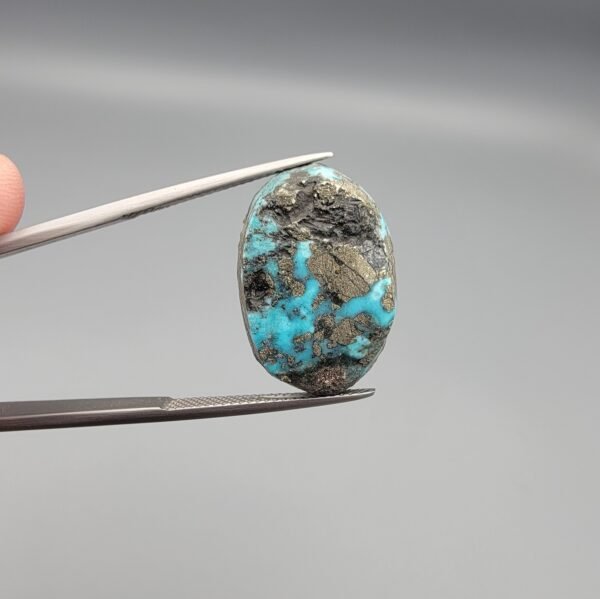 ​A 24.62-carat natural Iranian Turquoise (Feroza) from Kerman City, featuring a large oval cabochon cut with a vivid blue base and a beautiful web of metallic pyrite inclusions.