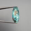 A 14.58-carat natural Iranian Turquoise (Feroza) from Kerman City, featuring an elegant oval cabochon cut with a vivid blue body and subtle metallic pyrite flecks, held in jeweler's tweezers.