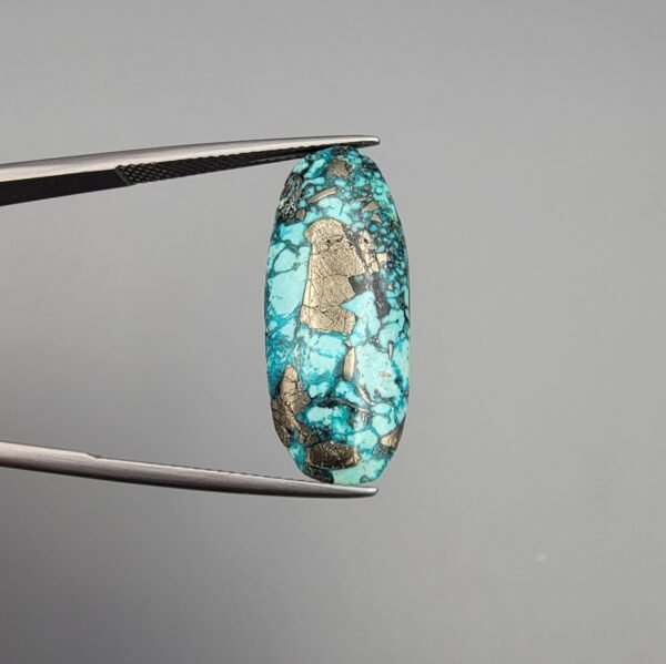 A 14.58-carat natural Iranian Turquoise (Feroza) from Kerman City, featuring an elegant oval cabochon cut with a vivid blue body and subtle metallic pyrite flecks, held in jeweler's tweezers.