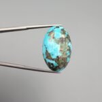 A massive 35.11-carat natural Iranian Turquoise (Feroza) from Kerman City, featuring a high-domed oval cabochon cut, saturated sky-blue color, and a brilliant golden pyrite matrix, shown from multiple angles.