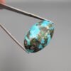 A massive 35.11-carat natural Iranian Turquoise (Feroza) from Kerman City, featuring a high-domed oval cabochon cut, saturated sky-blue color, and a brilliant golden pyrite matrix, shown from multiple angles.