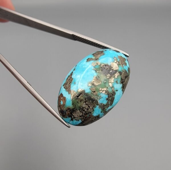 A massive 35.11-carat natural Iranian Turquoise (Feroza) from Kerman City, featuring a high-domed oval cabochon cut, saturated sky-blue color, and a brilliant golden pyrite matrix, shown from multiple angles.