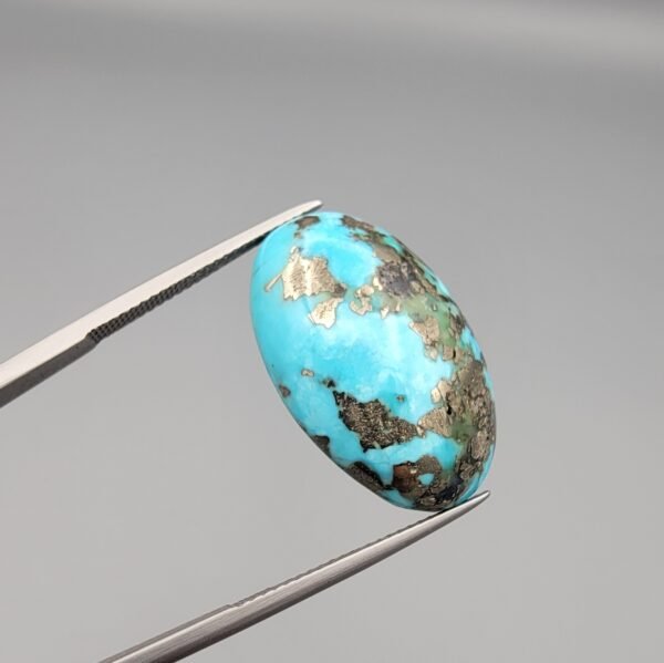 A massive 35.11-carat natural Iranian Turquoise (Feroza) from Kerman City, featuring a high-domed oval cabochon cut, saturated sky-blue color, and a brilliant golden pyrite matrix, shown from multiple angles.