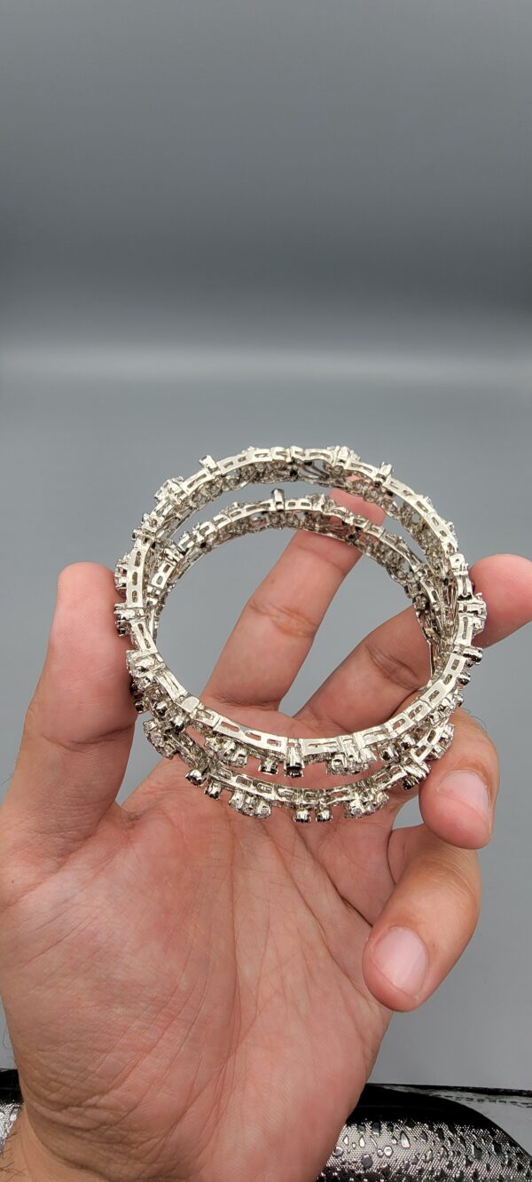 Pair of handcrafted pure silver bangles featuring a floral vine design set with black and white zircons, weighing 52.31 grams, held against a grey background.