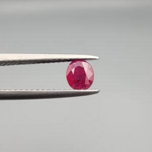 A 0.59 carat natural red Ruby (Yaqoot) from Kabul, Afghanistan, displaying a classic oval cut with rich red saturation and natural internal inclusions, held in jeweler's tweezers.