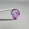 A 11.05-carat natural purple Amethyst (Katela) from Brazil, featuring a brilliant oval faceted cut with exceptional clarity and deep violet saturation, shown in jeweler's tweezers.