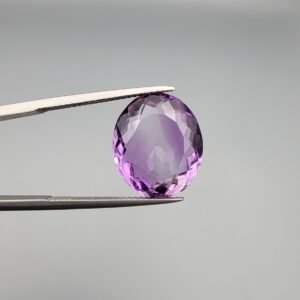 A 11.05-carat natural purple Amethyst (Katela) from Brazil, featuring a brilliant oval faceted cut with exceptional clarity and deep violet saturation, shown in jeweler's tweezers.