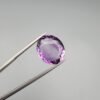 A 11.05-carat natural purple Amethyst (Katela) from Brazil, featuring a brilliant oval faceted cut with exceptional clarity and deep violet saturation, shown in jeweler's tweezers.
