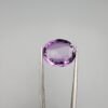 A 11.05-carat natural purple Amethyst (Katela) from Brazil, featuring a brilliant oval faceted cut with exceptional clarity and deep violet saturation, shown in jeweler's tweezers.