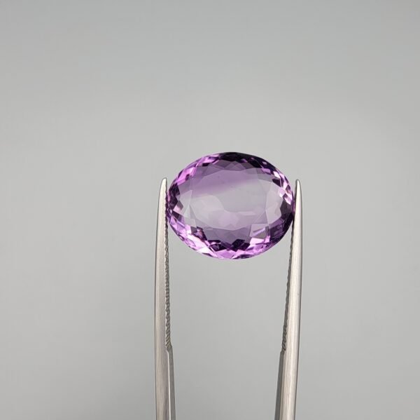 A 11.05-carat natural purple Amethyst (Katela) from Brazil, featuring a brilliant oval faceted cut with exceptional clarity and deep violet saturation, shown in jeweler's tweezers.