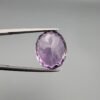​A 11.91-carat natural Brazilian Amethyst (Katela) gemstone, featuring a brilliant oval faceted cut with deep purple saturation and excellent clarity, held in jeweler's tweezers.
