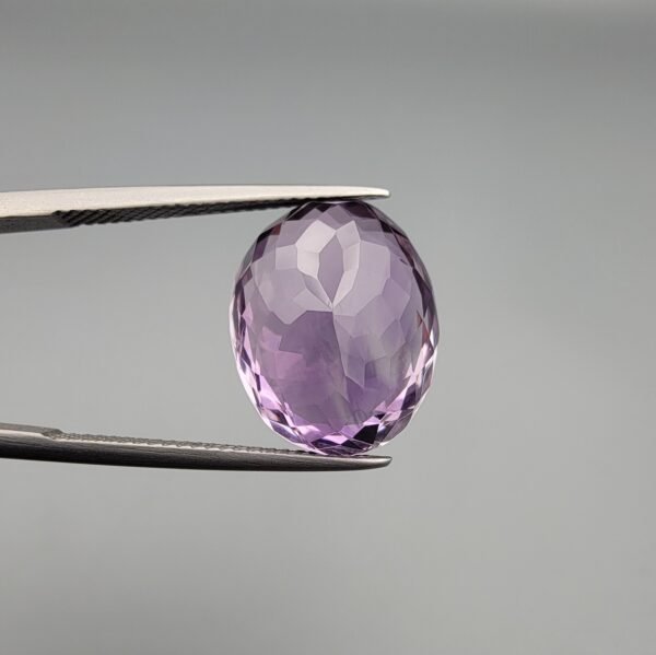 ​A 11.91-carat natural Brazilian Amethyst (Katela) gemstone, featuring a brilliant oval faceted cut with deep purple saturation and excellent clarity, held in jeweler's tweezers.