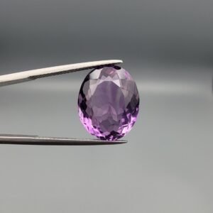 ​A 11.91-carat natural Brazilian Amethyst (Katela) gemstone, featuring a brilliant oval faceted cut with deep purple saturation and excellent clarity, held in jeweler's tweezers.