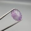 A large 13.51-carat natural Brazilian Amethyst (Katela) gemstone, showcasing a brilliant oval faceted cut with intense royal purple color and high transparency, held in jeweler's tweezers.