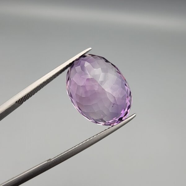 A large 13.51-carat natural Brazilian Amethyst (Katela) gemstone, showcasing a brilliant oval faceted cut with intense royal purple color and high transparency, held in jeweler's tweezers.