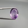 ​A 14-carat natural Brazilian Amethyst (Katela) gemstone, featuring a brilliant oval faceted cut with deep violet saturation and exceptional eye-clean clarity, held in jeweler's tweezers.