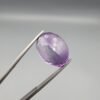 ​A 14-carat natural Brazilian Amethyst (Katela) gemstone, featuring a brilliant oval faceted cut with deep violet saturation and exceptional eye-clean clarity, held in jeweler's tweezers.