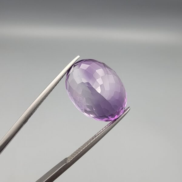 ​A 14-carat natural Brazilian Amethyst (Katela) gemstone, featuring a brilliant oval faceted cut with deep violet saturation and exceptional eye-clean clarity, held in jeweler's tweezers.