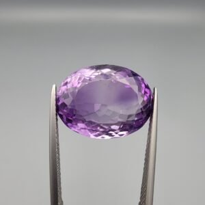 ​A 14-carat natural Brazilian Amethyst (Katela) gemstone, featuring a brilliant oval faceted cut with deep violet saturation and exceptional eye-clean clarity, held in jeweler's tweezers.