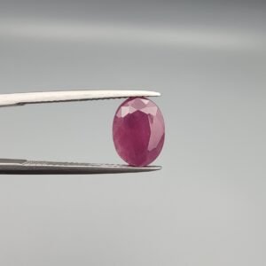 ​A 4.61-carat natural Mozambique Ruby (Yaqoot) gemstone, featuring a brilliant oval faceted cut with a rich pigeon-blood red hue and excellent transparency, held in jeweler's tweezers.