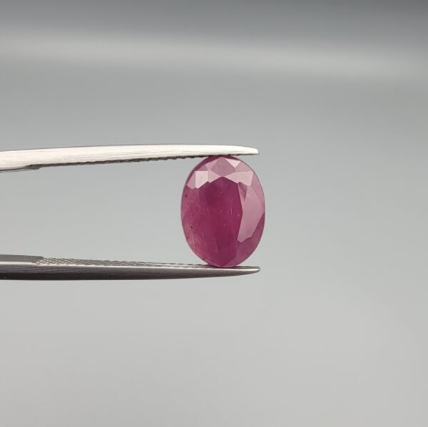 ​A 4.61-carat natural Mozambique Ruby (Yaqoot) gemstone, featuring a brilliant oval faceted cut with a rich pigeon-blood red hue and excellent transparency, held in jeweler's tweezers.