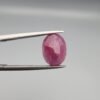 ​A 4.61-carat natural Mozambique Ruby (Yaqoot) gemstone, featuring a brilliant oval faceted cut with a rich pigeon-blood red hue and excellent transparency, held in jeweler's tweezers.