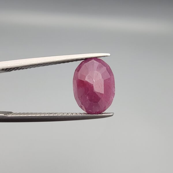 ​A 4.61-carat natural Mozambique Ruby (Yaqoot) gemstone, featuring a brilliant oval faceted cut with a rich pigeon-blood red hue and excellent transparency, held in jeweler's tweezers.