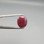 ​A 3.81-carat natural Mozambique Ruby (Yaqoot) gemstone in a brilliant oval faceted cut, displaying a rich red color with natural black silk inclusions that remain eye-clean, held in jeweler's tweezers.