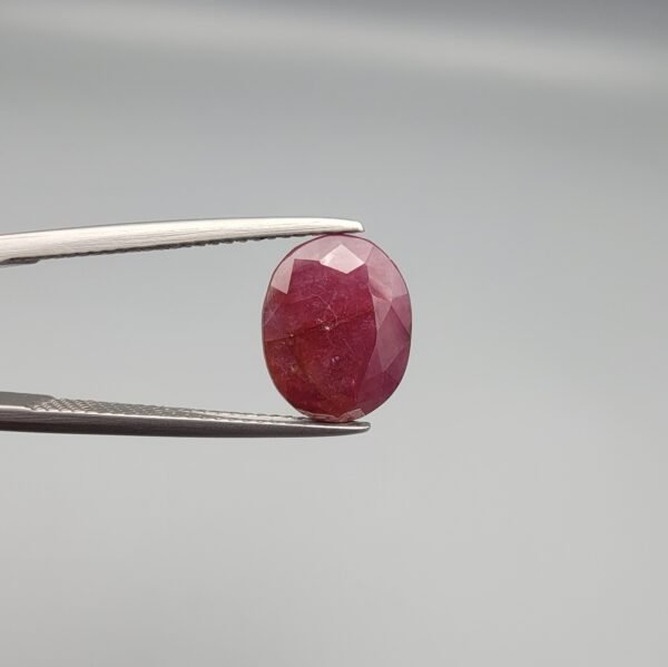 ​A 3.81-carat natural Mozambique Ruby (Yaqoot) gemstone in a brilliant oval faceted cut, displaying a rich red color with natural black silk inclusions that remain eye-clean, held in jeweler's tweezers.