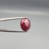 ​A 3.81-carat natural Mozambique Ruby (Yaqoot) gemstone in a brilliant oval faceted cut, displaying a rich red color with natural black silk inclusions that remain eye-clean, held in jeweler's tweezers.