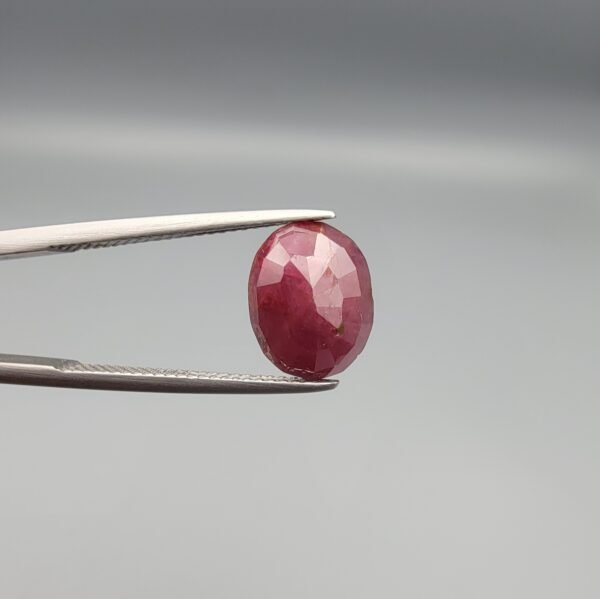 ​A 3.81-carat natural Mozambique Ruby (Yaqoot) gemstone in a brilliant oval faceted cut, displaying a rich red color with natural black silk inclusions that remain eye-clean, held in jeweler's tweezers.