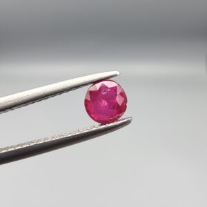 A 0.43-carat natural red Ruby (Yaqoot) from Kabul, Afghanistan, featuring a round cut with visible natural mountain cracks and surface textures, held in jeweler's tweezers.