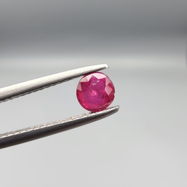 A 0.43-carat natural red Ruby (Yaqoot) from Kabul, Afghanistan, featuring a round cut with visible natural mountain cracks and surface textures, held in jeweler's tweezers.