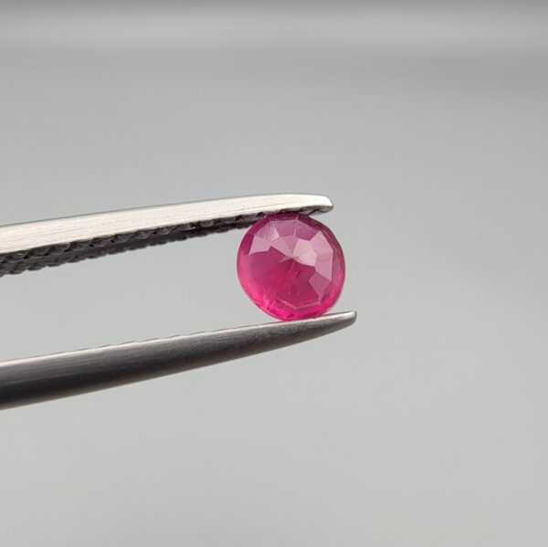 A 0.43-carat natural red Ruby (Yaqoot) from Kabul, Afghanistan, featuring a round cut with visible natural mountain cracks and surface textures, held in jeweler's tweezers.
